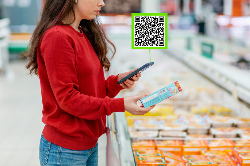 a young caucasian woman scans the qr code on the packaging of a semi finished product using smartphone. in the background is a supermarket. concept of modern technologies and shopping